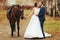 Groom kisses a bride while she holds a harness on the horse