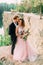 Groom is kissing his bride. Happy newlyweds embracing. Man in tuxedo and woman in a pink wedding dress is posing on