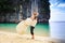 Groom lifts blonde curly bride in fluffy dress on beach