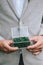 Groom in a light jacket holds the glass holding jewerly box with moss and wedding ring. Close up