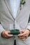 Groom in a light jacket holds the glass holding jewerly box with moss and wedding ring. Close up