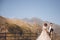 Groom in modern suit and bride in charming pink dress pose on the terasse with great mountain view in Georgia