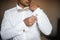 Groom morning preparation. Young bearded groom getting dressed in wedding shirt with wooden bow tie