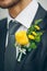 Groom\'s hand arranging yellow boutonniere flower on suit