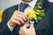 Groom\'s hand arranging yellow boutonniere flower on suit
