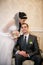 Groom sits in a chair and the bride stands near groom and kiss him in the room