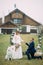 The groom stands on one knee in front of his bride next to dog and a wedding arch