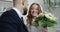 The groom in a suit gives a bouquet of roses to the young bride.