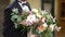 The groom in a suit holds a bouquet of the bride