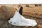 The groom, tearing his shirt, stands behind the bride, near a bale of hay.