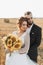 The groom, tearing his shirt, stands behind the bride, near a bale of hay.