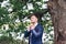 The groom on the wedding day is standing under a tree and straightening a bowtie