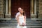 Groom in white clothes hugs the bride against the background of the Catholic Church