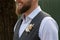 The groom in a white shirt, a butterfly and a plaid vest straightens his buttonhole. A young man with a beautiful boutonniere in