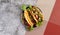 Ground beef tacos with lettuce, tomatoes, pink onions on a round plate on a dark gray background