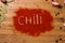 Ground chili peppers are scattered with the words `Chili` on a wooden background. View from above. Seasonings for meat and spicy