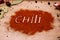 Ground chili peppers are scattered with the words `Chili` on a wooden background. View from above. Seasonings for meat and spicy