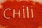 Ground chili peppers are scattered with the words `Chili` on a wooden background. View from above. Seasonings for meat and spicy