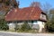 Ground floor abandoned family house with long wooden porch and high rusted metal roof overgrown with crawler plants and tall trees