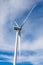 Ground low view on wind propeller turbine, blue sky, and clouds.