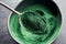 Ground spirulina algae on a spoon above a bowl
