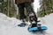 A ground view and closeup of the legs and feet of a person wearing nice snowshoes as they walk with the beautiful winter landscape