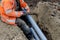 Groundworker in hi-viz coat cutting grey plastic telecom duct with hand saw while sitting