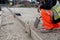 Groundworker in orange safety hi vis trousers fixing a timber along string line with steel pin to form a kerb riser