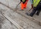 Groundworker in orange safety hi vis trousers fixing a timber along string line with steel pin to form a kerb riser