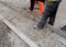 Groundworker in orange safety hi vis trousers fixing a timber along string line with steel pin to form a kerb riser