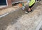 Groundworker placing and levelling with the shovel a semi-dry concrete around edging kerb during footpath construction