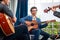 A group of Asian musicians playing guitar and violin sitting on classical music.