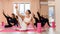 A group athletic women doing pilates or yoga on pink mats in front of a window in a beige loft studio interior. Teamwork