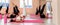 A group athletic women doing pilates or yoga on pink mats in front of a window in a beige loft studio interior. Teamwork