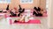 A group athletic women doing pilates or yoga on pink mats in front of a window in a beige loft studio interior. Teamwork