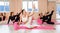 A group athletic women doing pilates or yoga on pink mats in front of a window in a beige loft studio interior. Teamwork