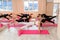 A group athletic women doing pilates or yoga on pink mats in front of a window in a beige loft studio interior. Teamwork