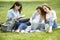 Group of attractive young people preparing for the exam with study book and a laptop sitting on the lawn. Student group and tutori