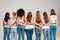 Group of beautiful diverse young women wearing white shirt and denim jeans putting arms around each other while posing