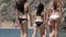Group of beautiful girls in bikinis walking on the shore of the beach, the view from the back