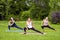 Group of beautiful healthy slimy woman doing exersices on mat in the green grass in the park, streching legs, looking at camera