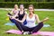 Group of beautiful healthy slimy women doing exersices on the green grass in park, siting in lotus poses and meditation, looking