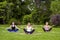 Group of beautiful healthy slimy young women doing exersices on the green grass in the park, siting in lotus poses and meditation