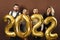 Group of beautiful well dressed party people celebrating arrival of 2022 New Year with a golden balloons