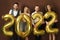 Group of beautiful well dressed party people celebrating arrival of 2022 New Year with a golden balloons