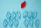 A group of blue paper boats heading in one direction and one red one heading in the opposite direction. The concept of