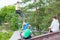 A group of boys hanging out on a skateboarding ramp ride a bicycle and scooters, one guy performs a trick by bouncing in the air