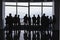 Group of business people standing in front of wide panaramic office windows. Silhouettes of different groups of businesspeople tal