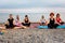 Group of Caucasian women meditate sitting on sports mats on pebble beach. Copy space. Yoga and wellness