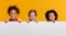 Group of cheerful happy multinational children with blank white poster on yellow background